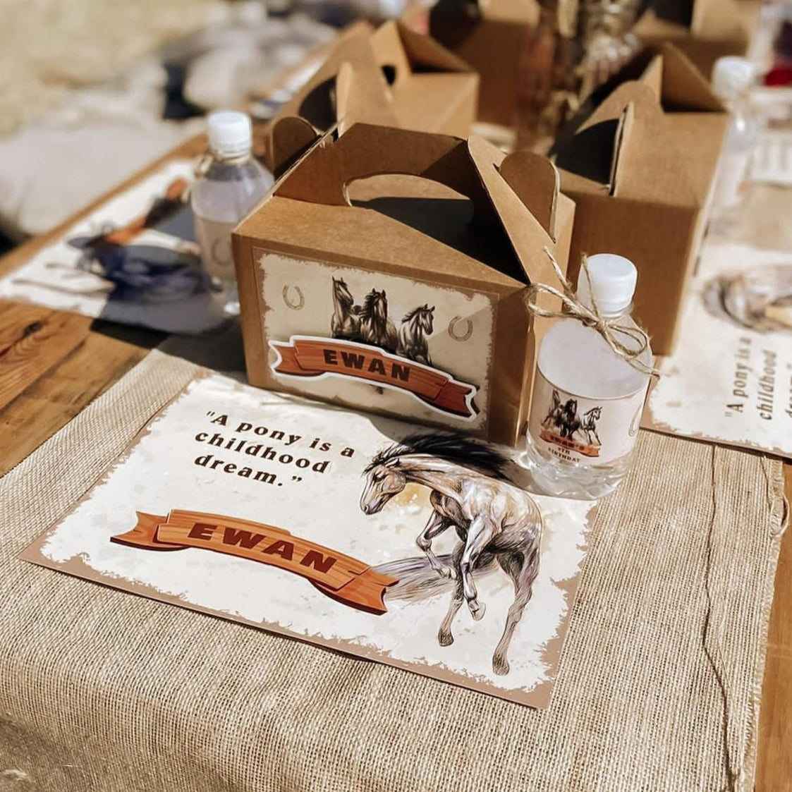 Table setting with 'Ewan' branded items including a box, bottle, and horse figurine on a rustic table.