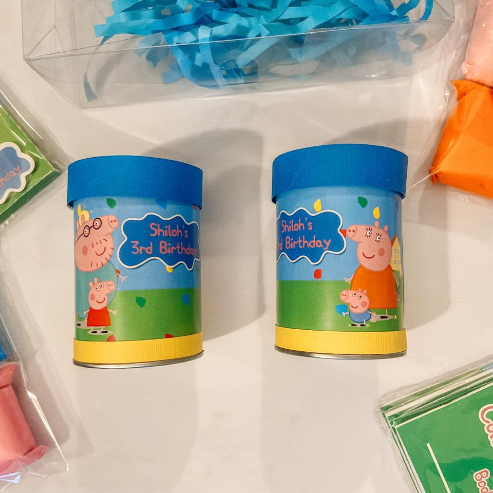 Peppa Pig-themed party favor items including small containers and a coloring book on a white surface.